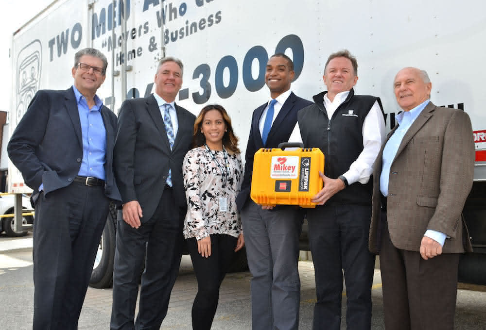 Every TWO MEN AND A TRUCK® moving vehicle in Canada sports a Mikey defibrillator with drivers and movers trained to use them. Toronto East franchise Owner Paul Bolté  (holding the defibrillator) takes pride in supporting The Mikey Network, the company’s charity of choice. Photo: Nicola Betts