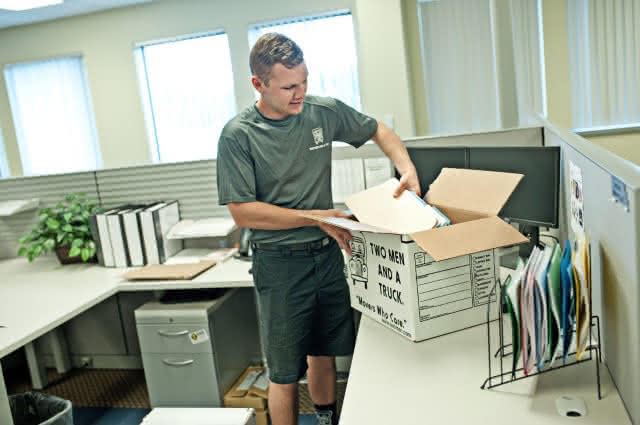 Two Men and a truck employee packing office goods in to a box